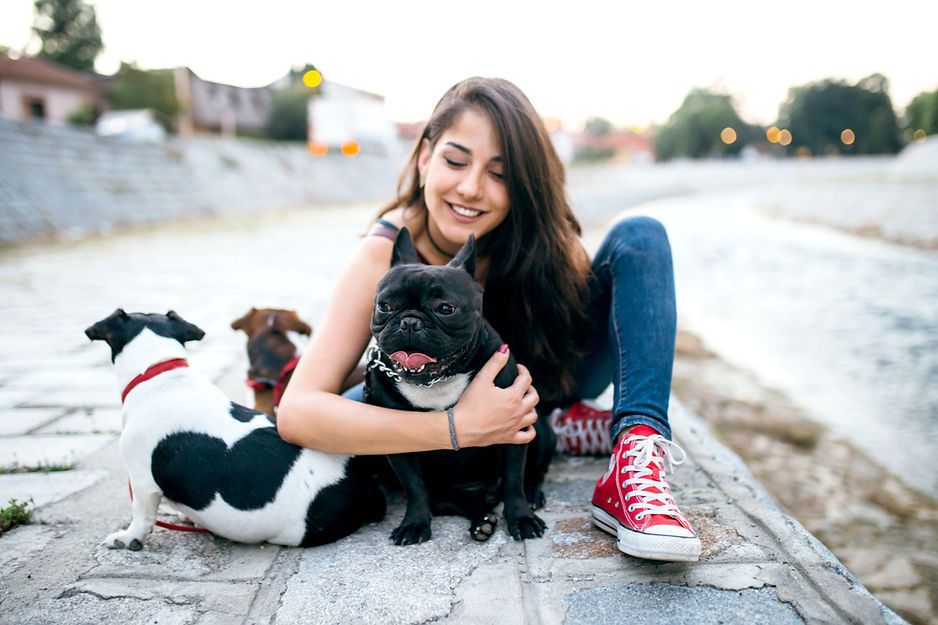 A woman is sitting on the ground with three dogs.