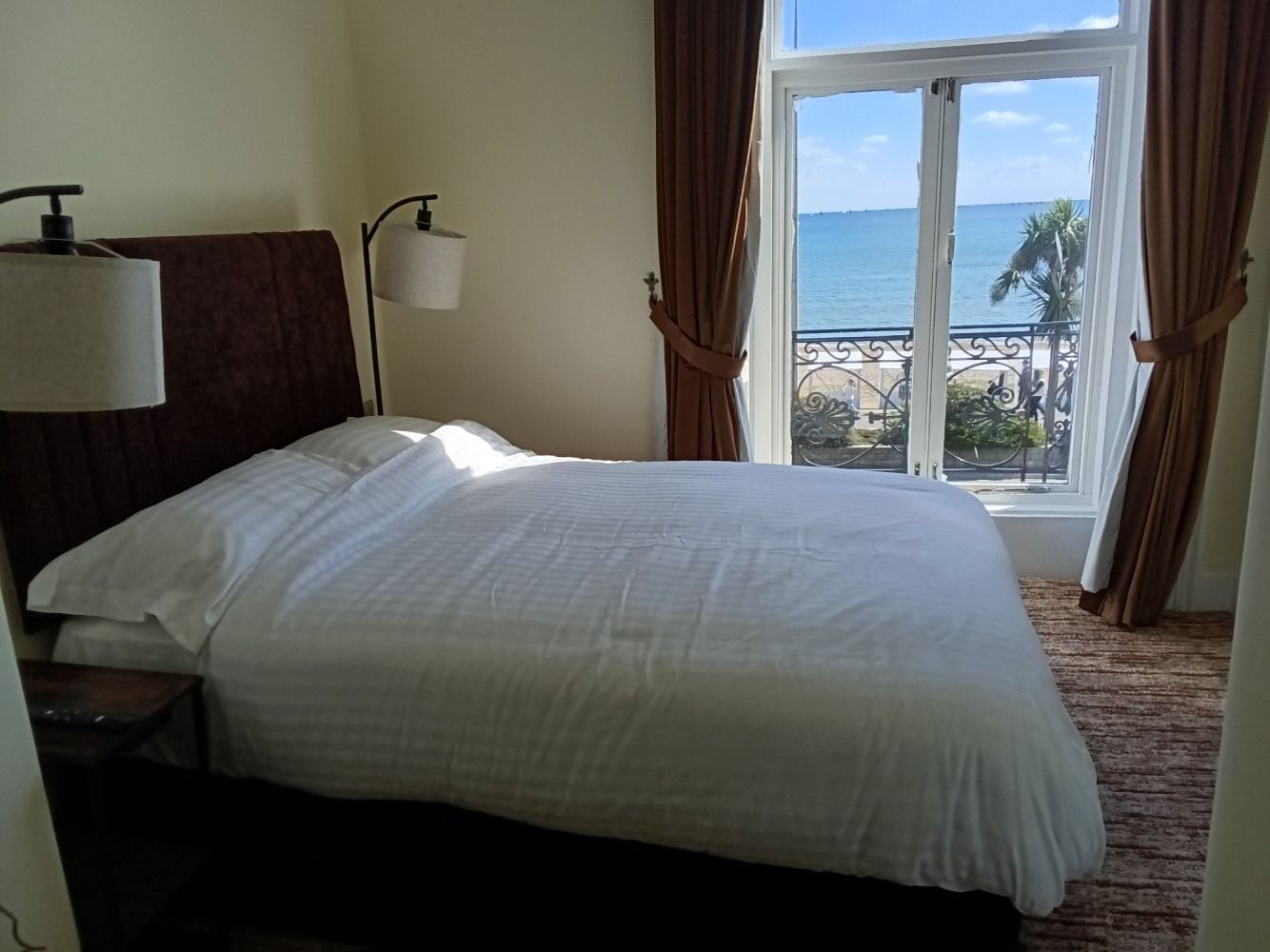 Bedroom with a large bed, brown headboard, and window overlooking the ocean.