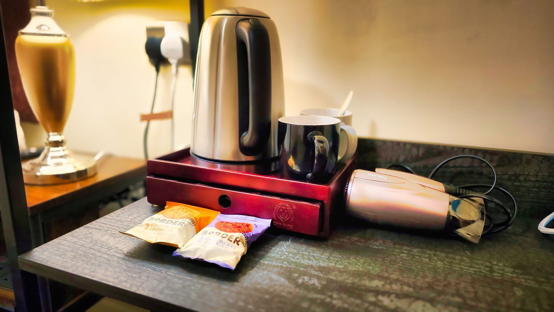 Kettle, mugs, and tea bags on a counter in a hotel room.