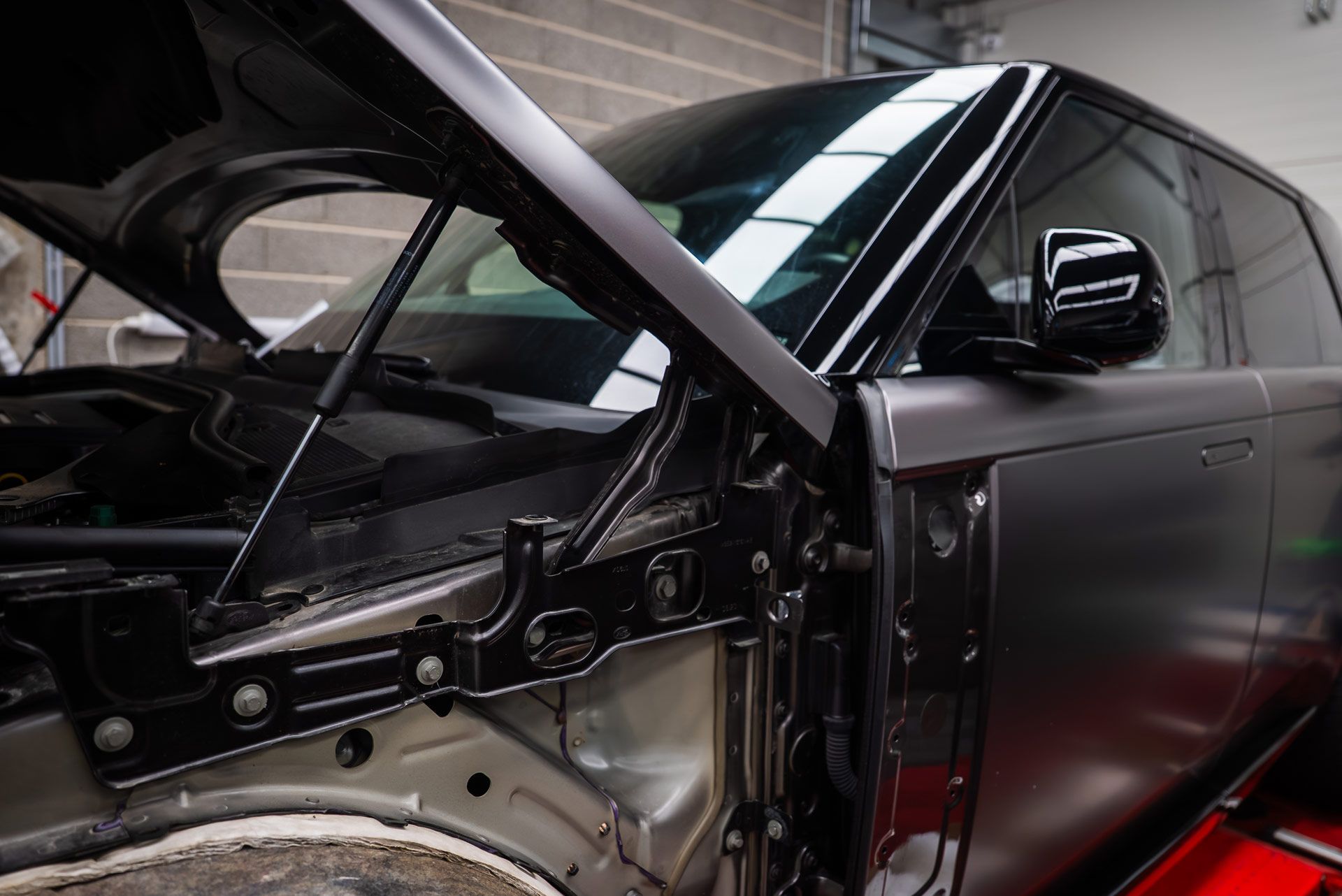 Black car with hood open, in a workshop, possibly being wrapped in matte vinyl.