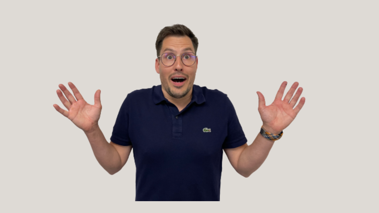 Mann im blauen Poloshirt mit überraschtem Gesichtsausdruck, erhobenen Armen und Brille.