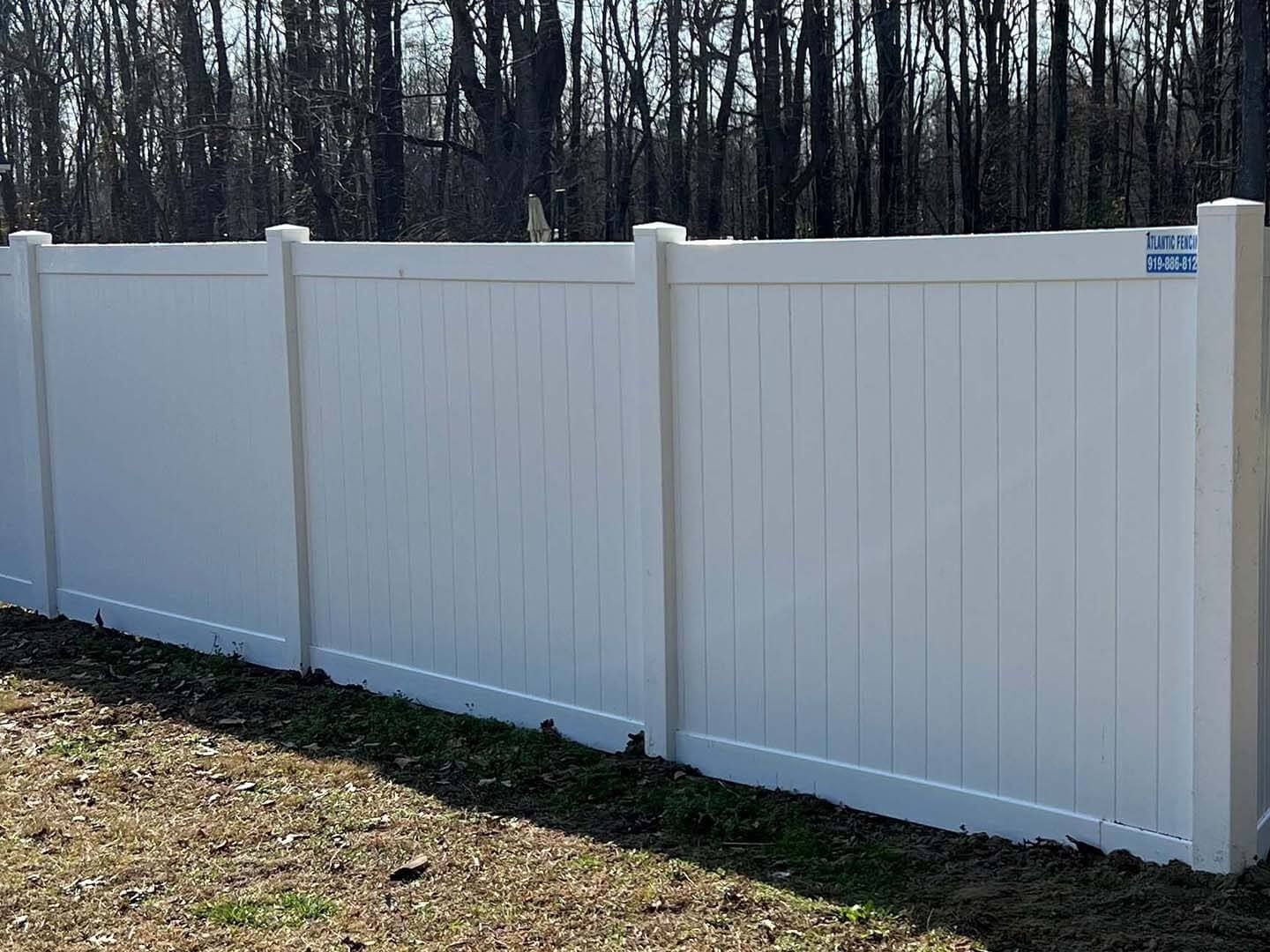 White vinyl privacy fence in a yard, with trees in the background.