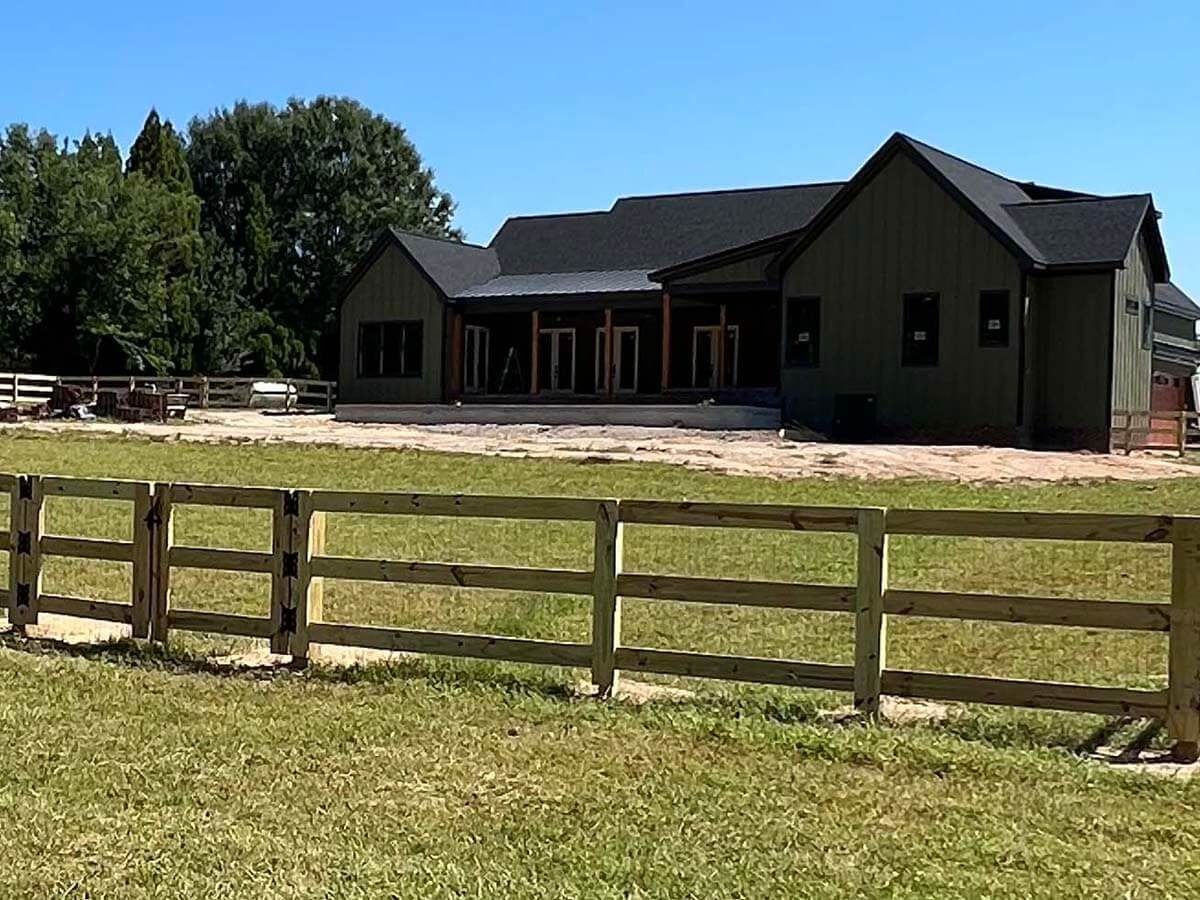 Green house with wooden fence in front, set in grassy yard.