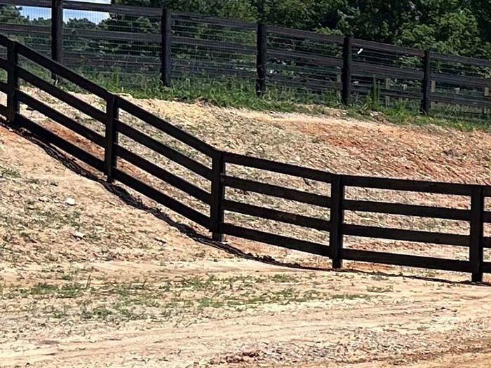 Dark brown wooden fence curving around a grassy hillside.