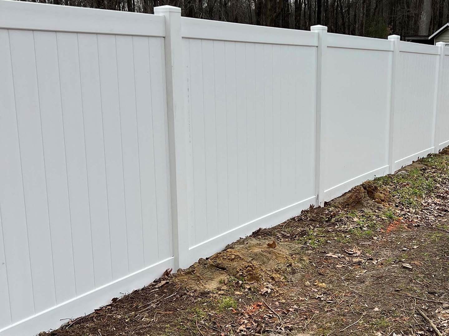 White vinyl fence in a yard with bare ground.