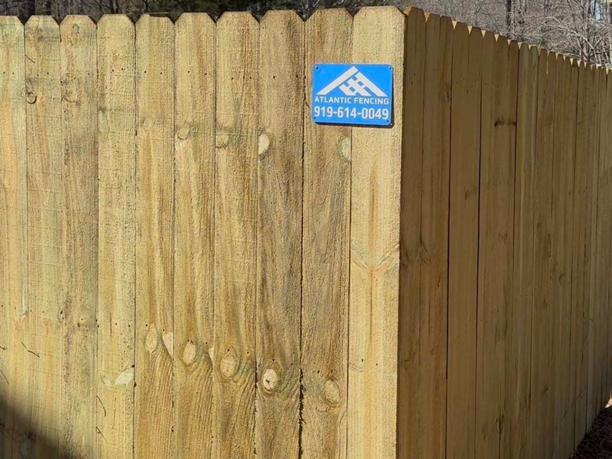 Wooden fence with a blue contractor sign on the corner.