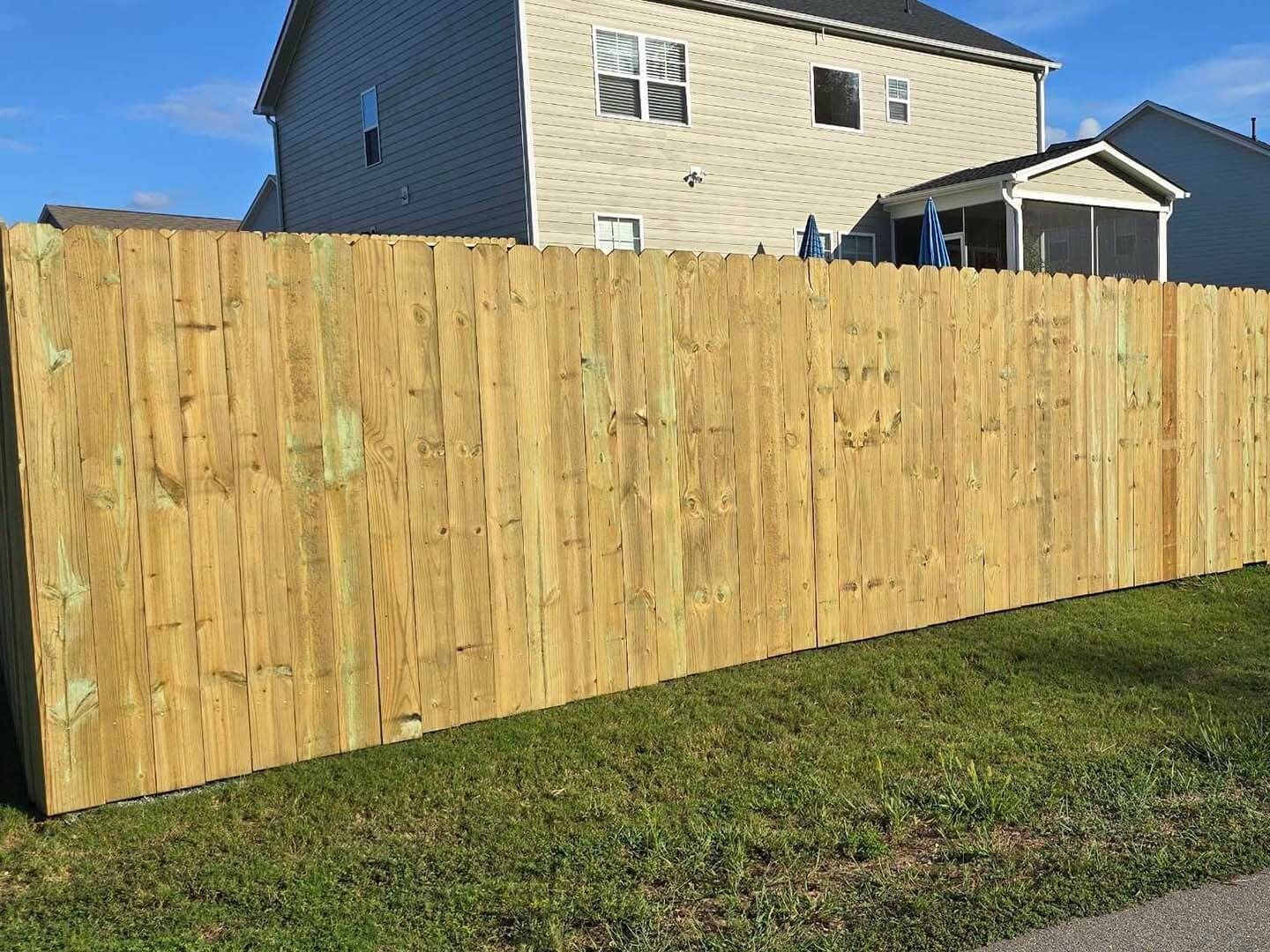 Wooden fence in front of a house, green grass, and blue sky.