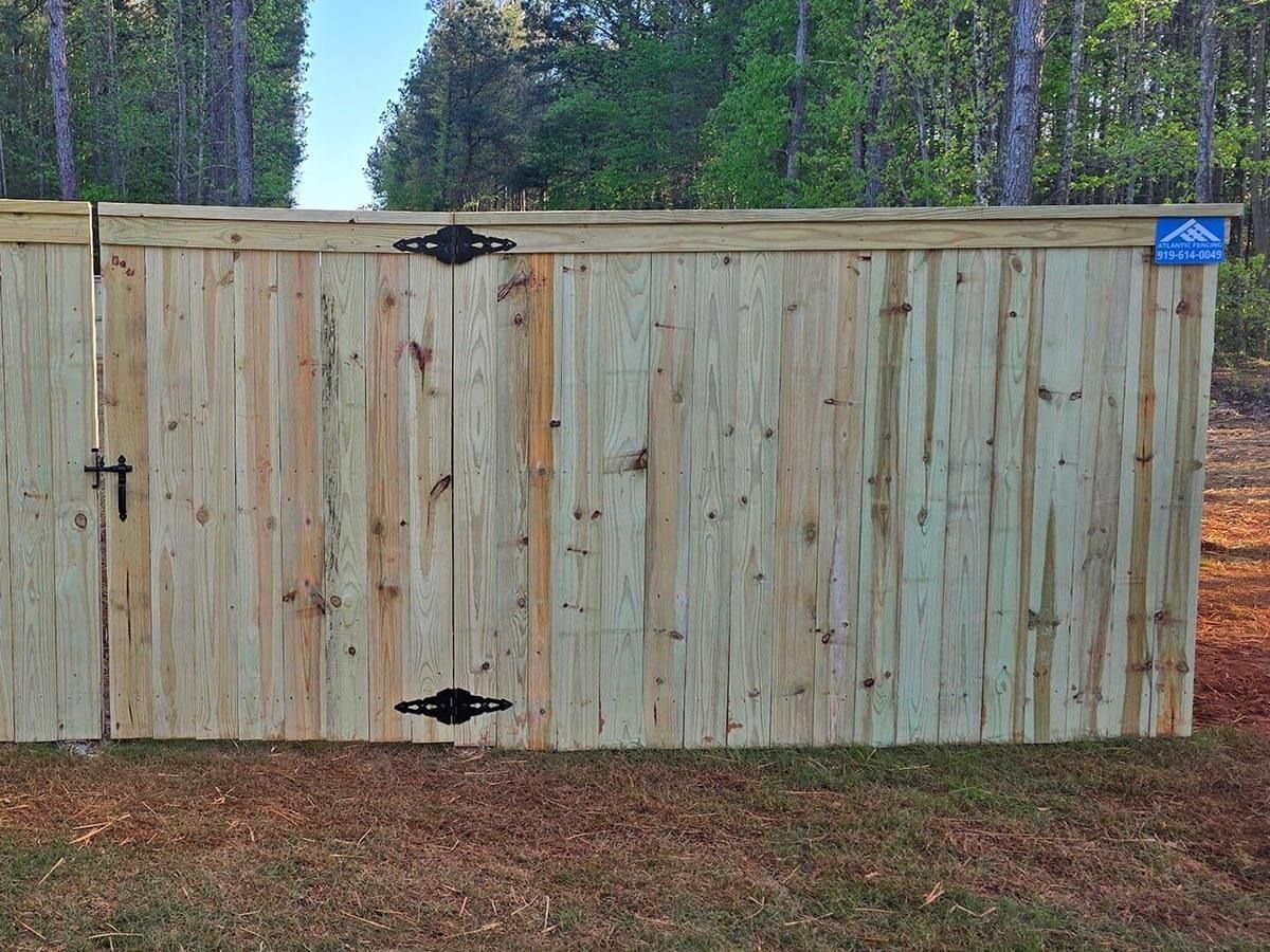 Wooden gate with black hardware in a grassy yard, surrounded by trees.