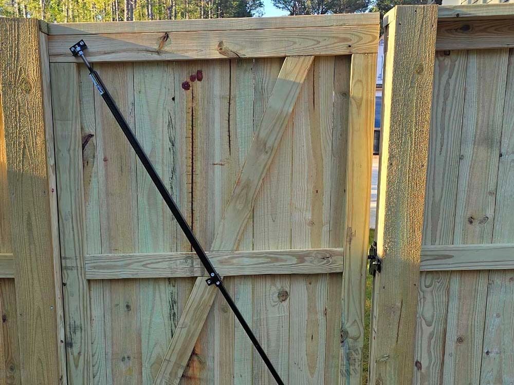 Wooden gate with diagonal bracing, black gate closer, and hinges, set in a wooden fence.
