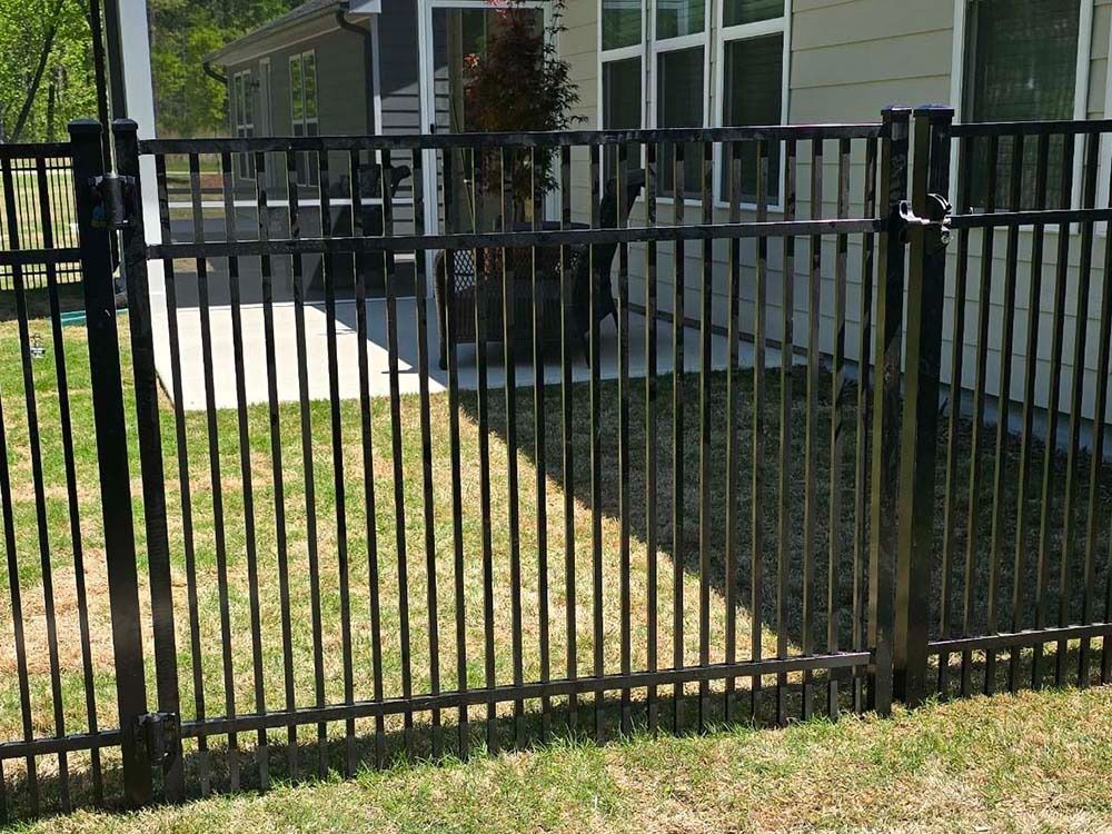Black metal fence in a grassy yard, with a house in the background.