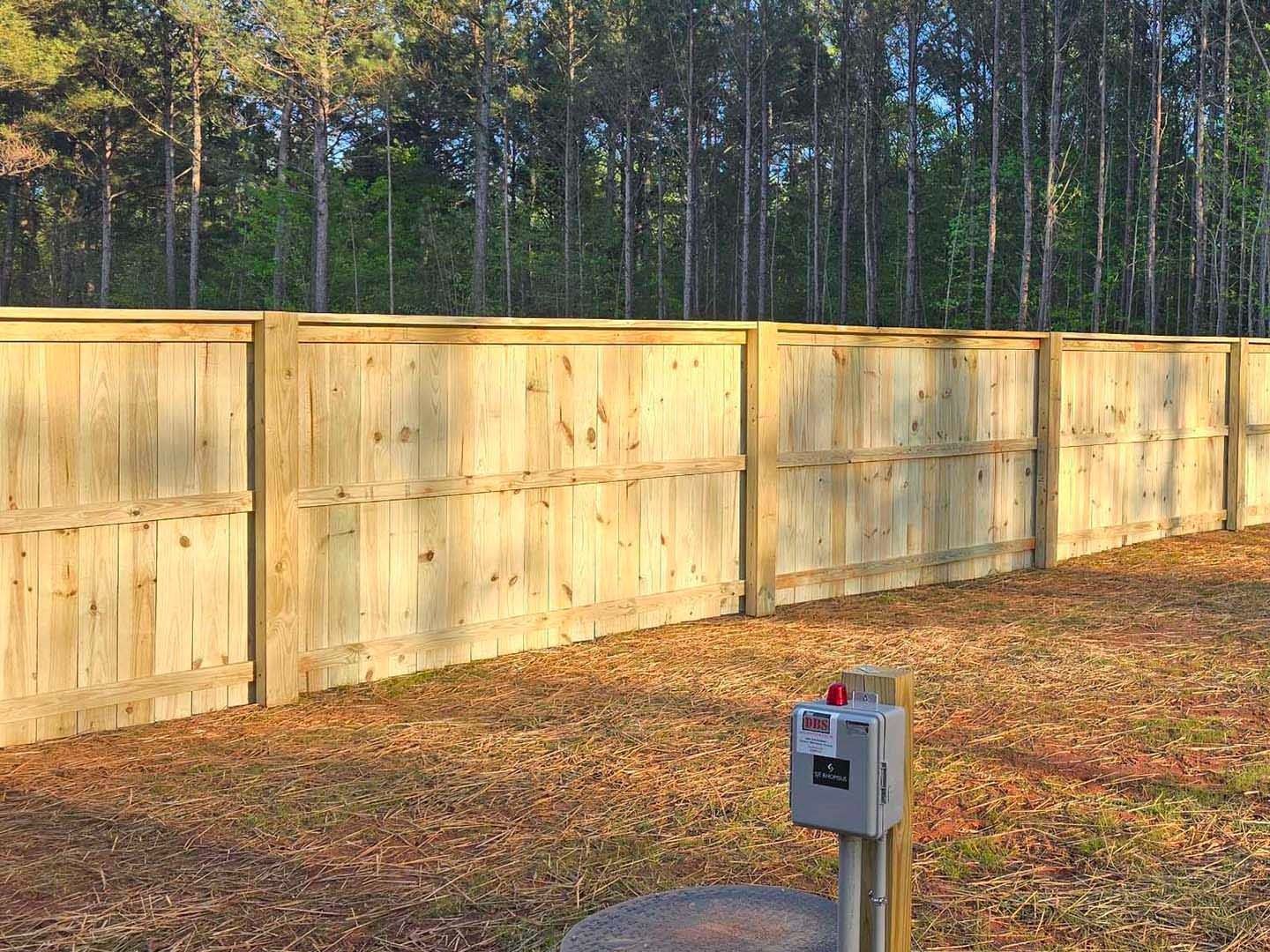 Wooden fence in a yard, with trees in the background and a mailbox in the foreground.