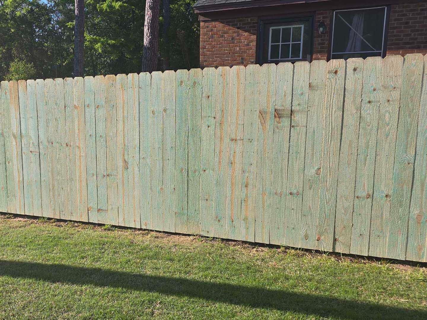 Old, weathered green wooden fence with some missing paint, in front of green grass.