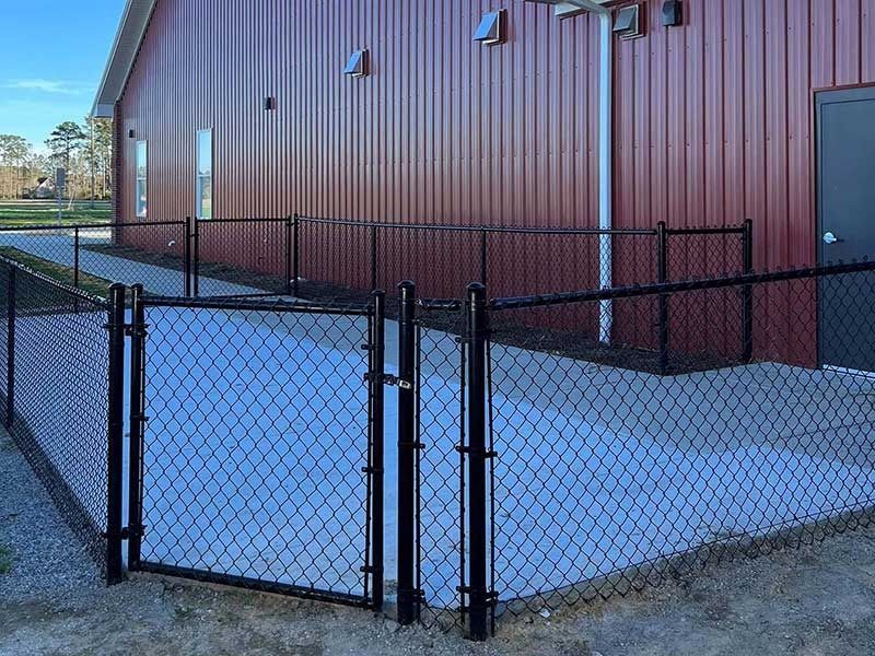 Black chain-link fence around a concrete patio next to a maroon metal building with a black door.