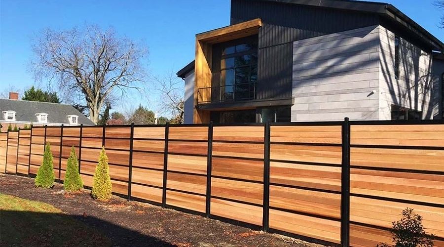 Modern horizontal wood privacy fence with black metal posts enclosing a modern home property.