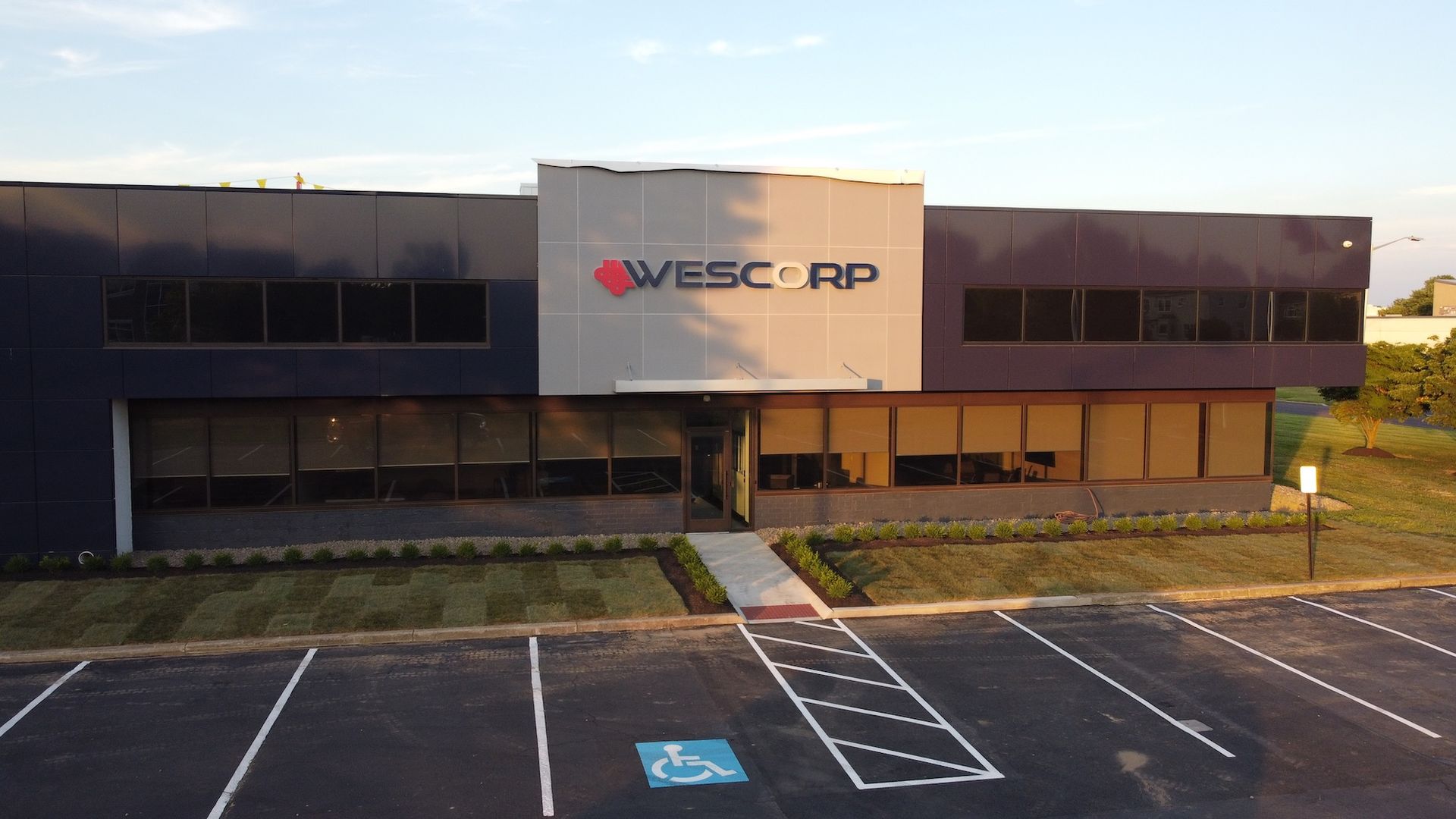 Exterior view of the WESCORP building with a blue and grey facade, a parking lot, and a handicap parking space.