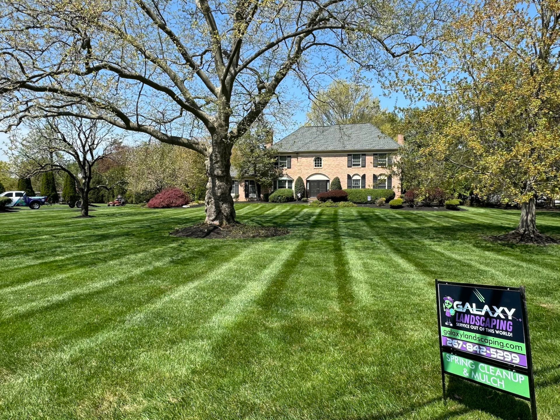 Lawn with striped pattern in front of a large house, with a sign for a lawn care business.