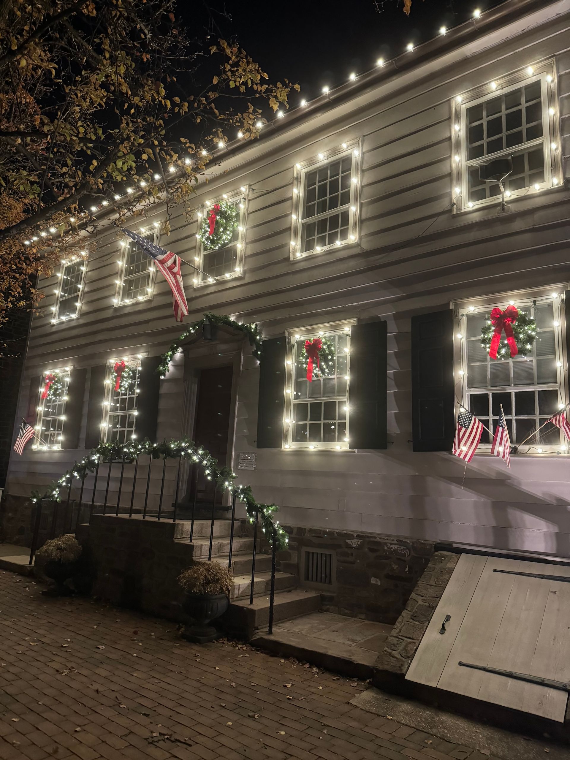 White house with Christmas lights framing windows, wreaths, and string lights on the steps at night.