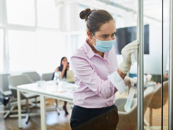 A woman wearing a mask and gloves is cleaning a door in an office.