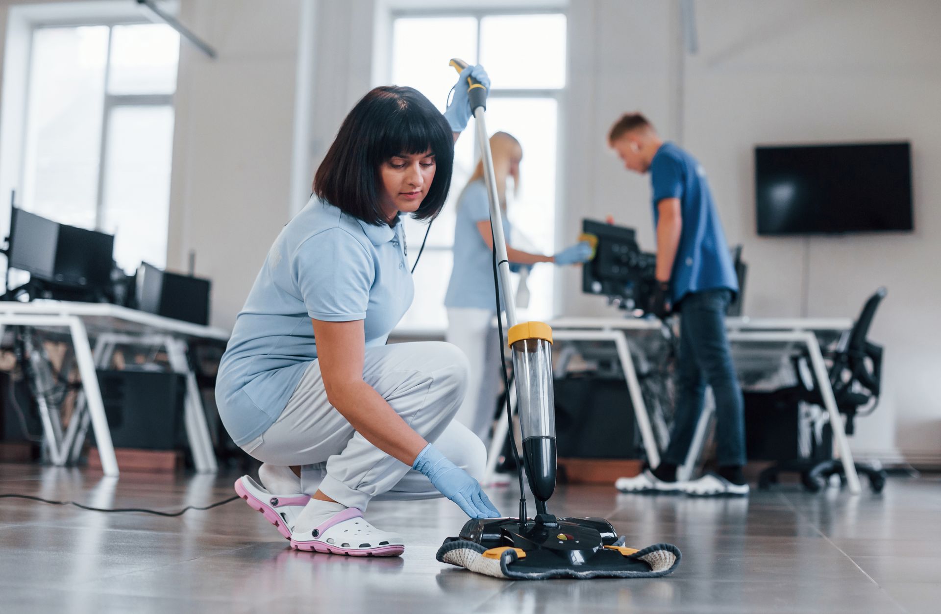 A woman is cleaning the floor of an office with a mop.