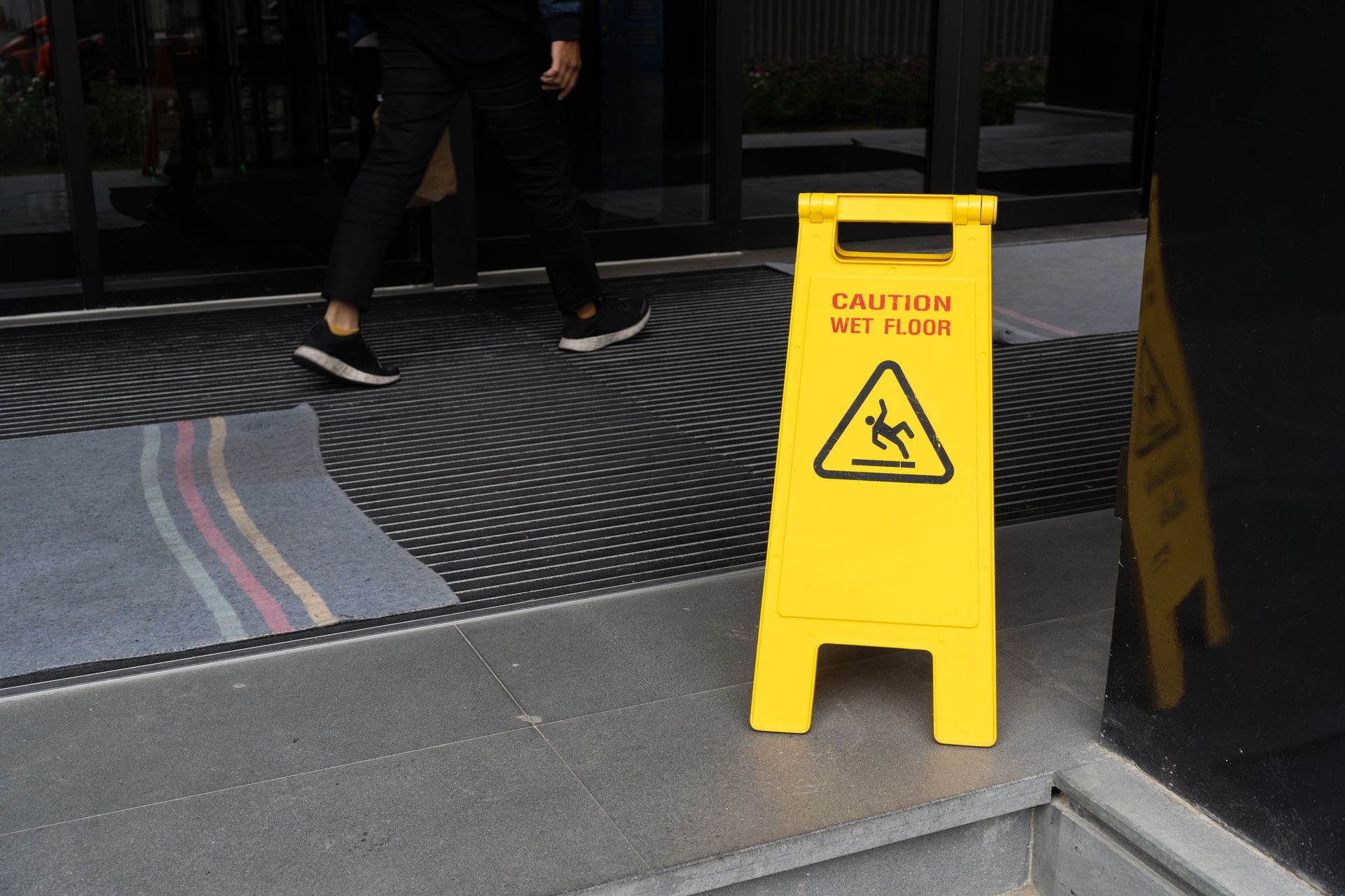 A person is walking past a yellow caution sign on the sidewalk.