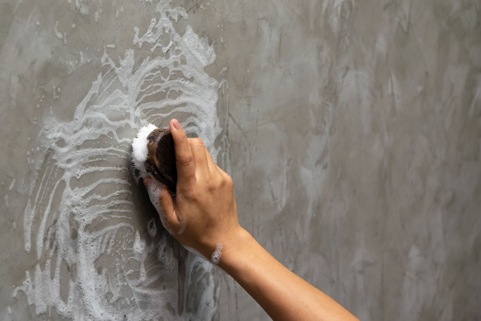 A person is cleaning a concrete wall with a sponge.