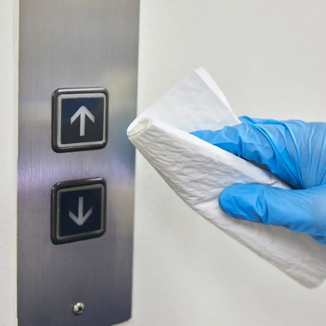Gloved cleaner disinfecting high-touch elevator buttons in a Greenville facility