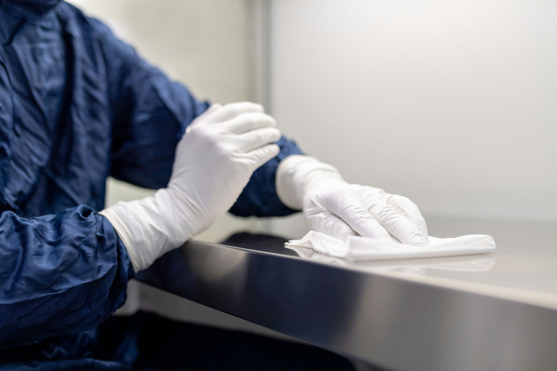 A person wearing gloves is cleaning a stainless steel table with a cloth.