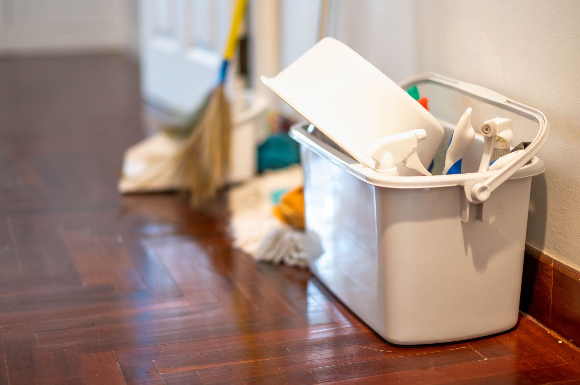 A white bucket filled with cleaning supplies is sitting on a wooden floor.