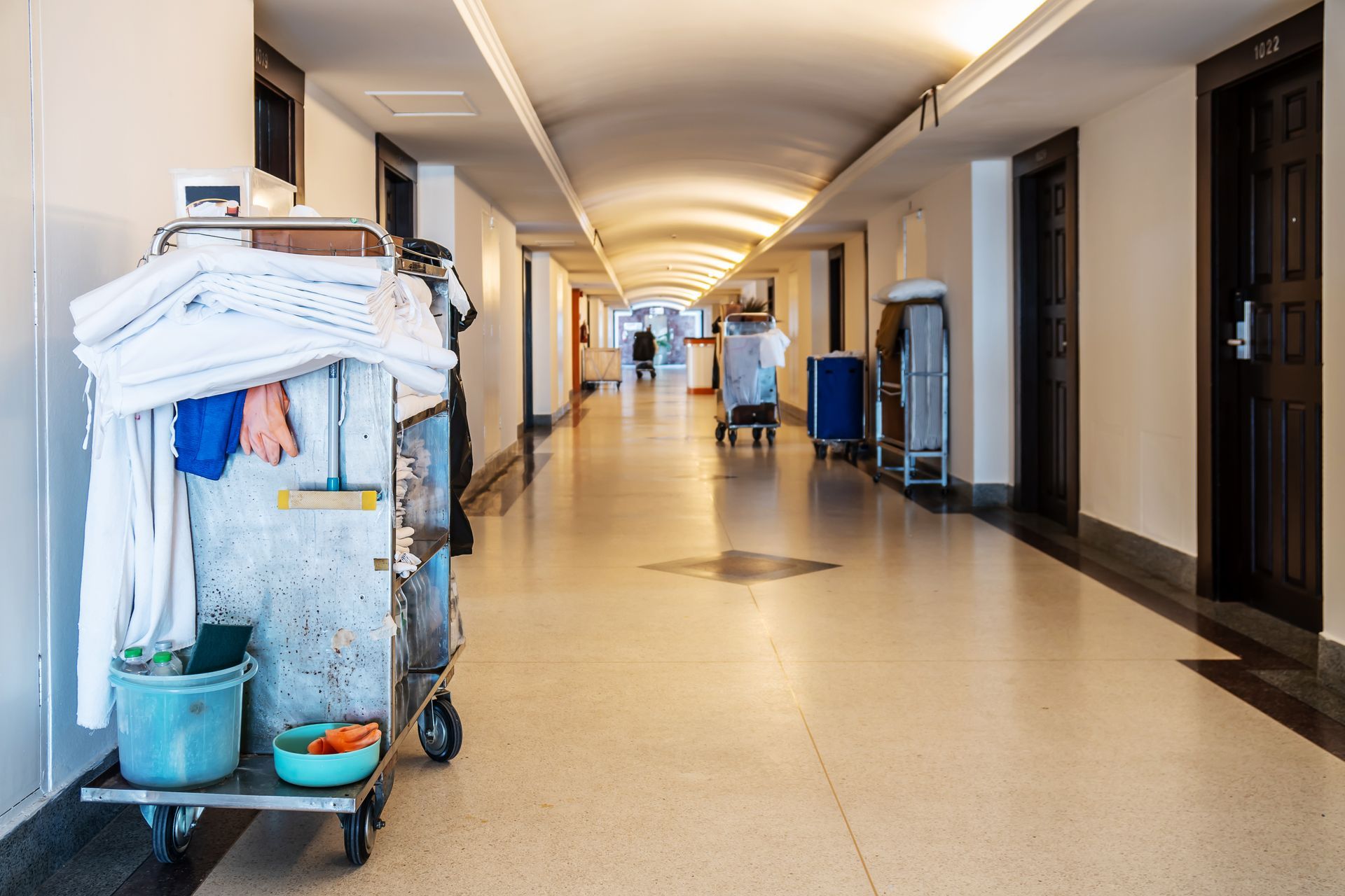 A cleaning cart is sitting in the middle of a long hallway.
