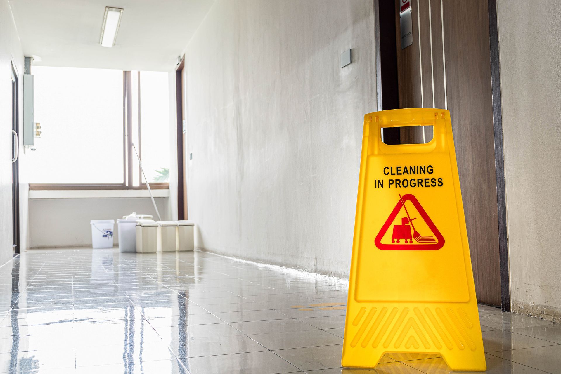A yellow caution sign is sitting on the floor in a hallway.