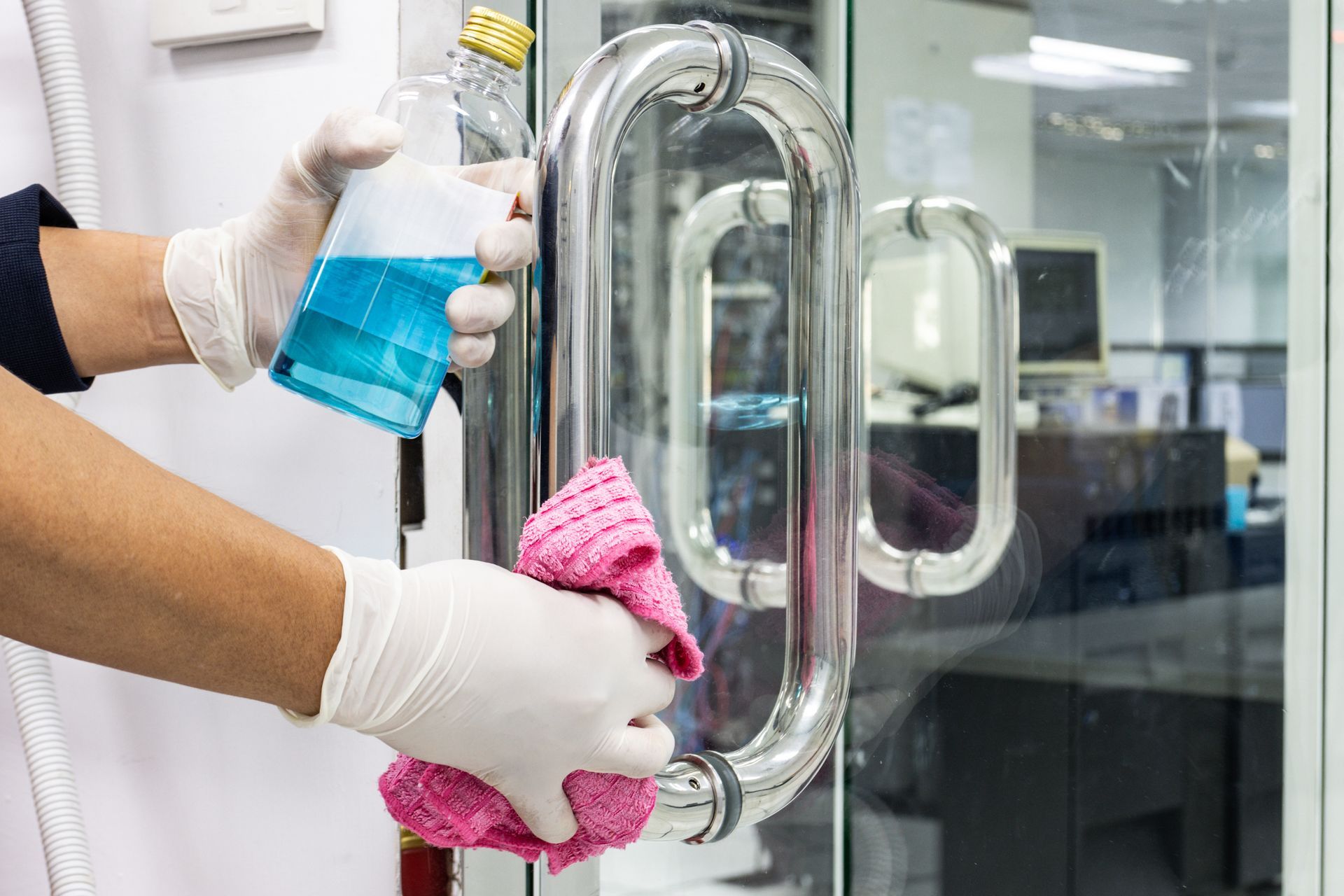 A person is cleaning a door handle with a cloth and spray bottle.