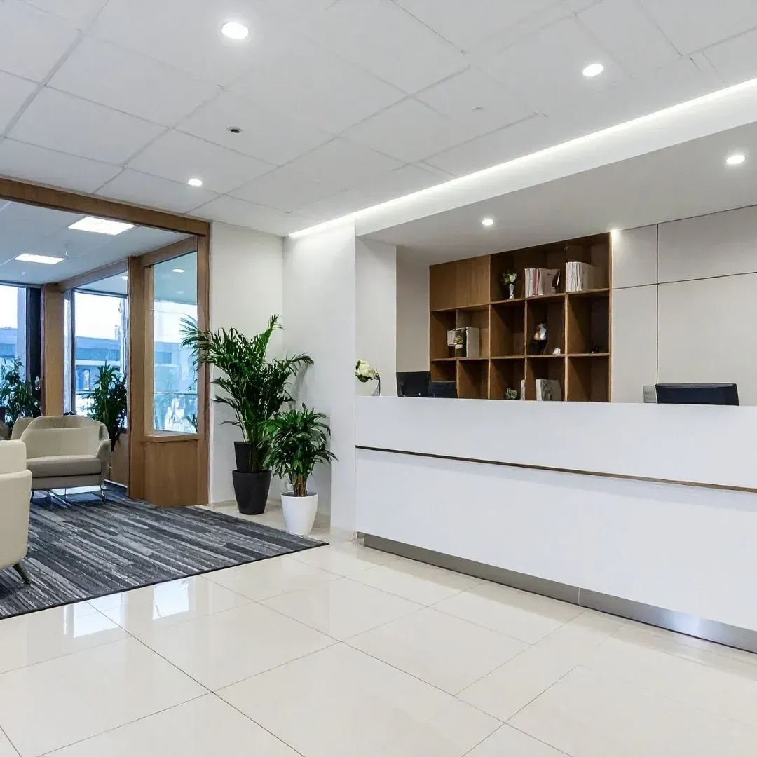Bright modern office lobby with white reception desk, potted plant, seating area, and large windows