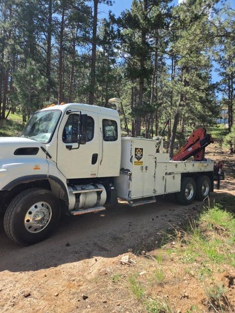White tow truck with red crane parked on a dirt road in a pine forest