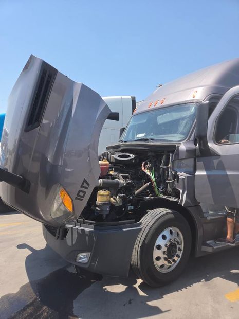 Semi-truck with its hood open, exposing the engine on a sunny road.