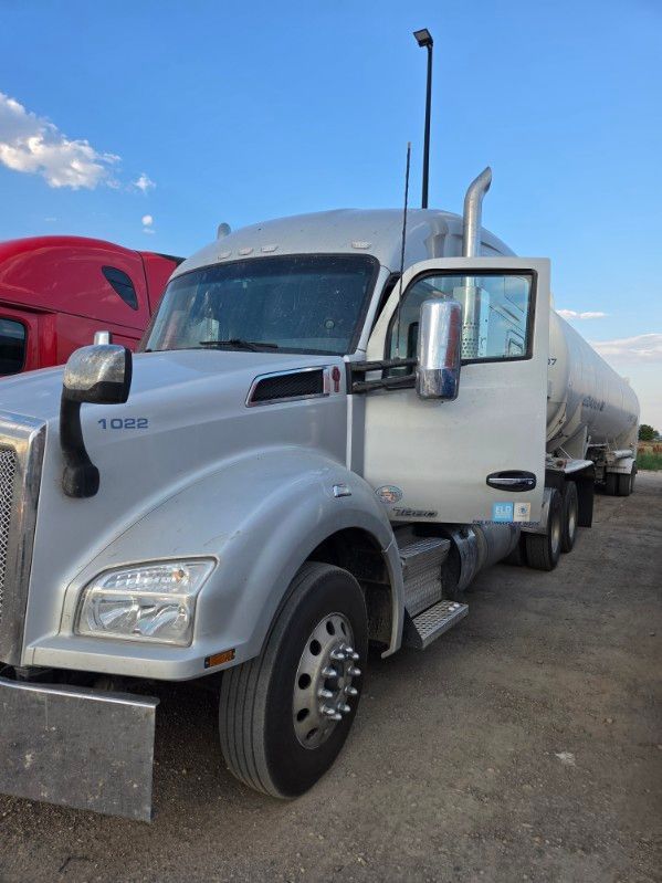 Silver dump truck parked outdoors beside a red truck under a blue sky