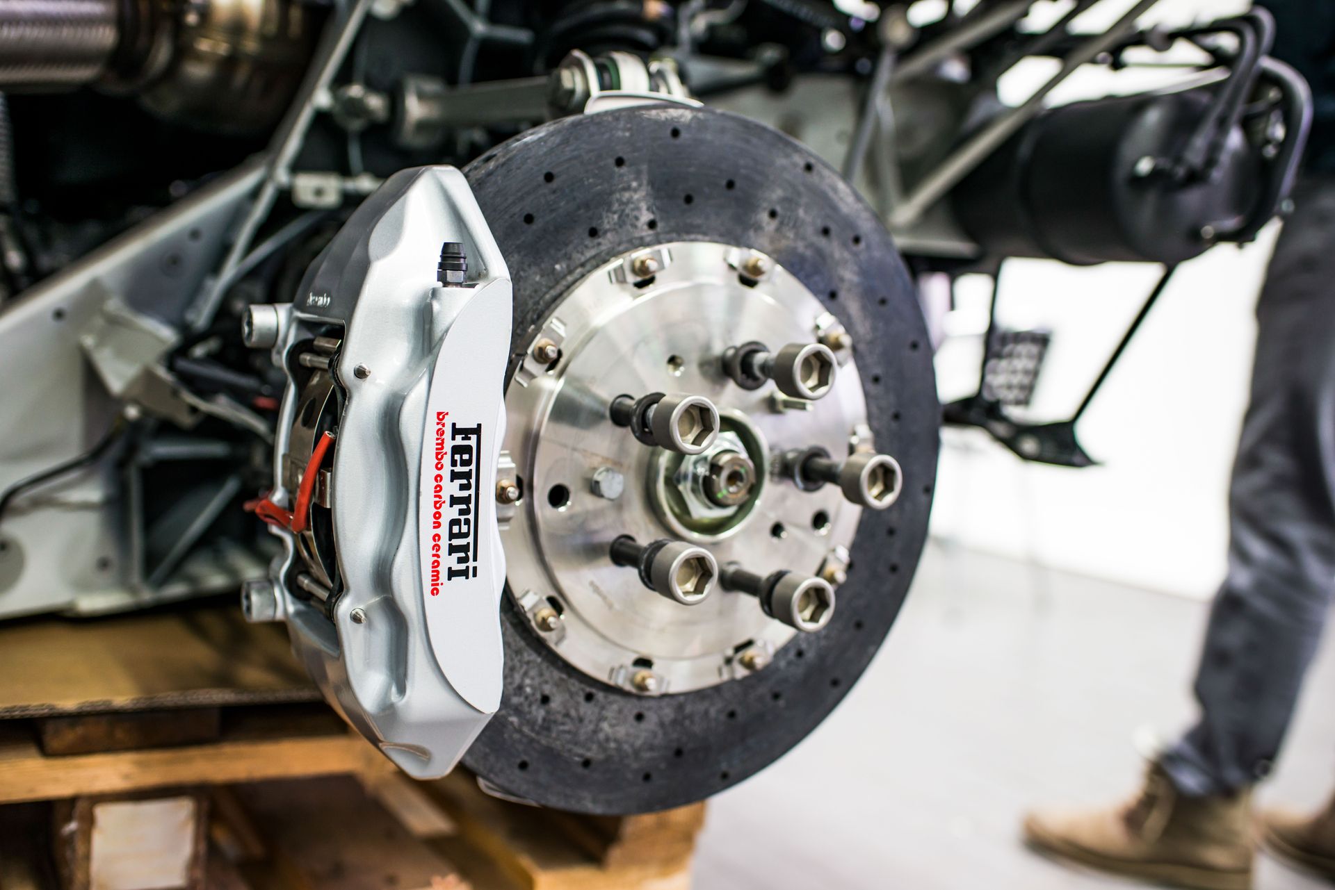 Close-up of a car brake rotor and silver caliper on a vehicle chassis, with a person in the background