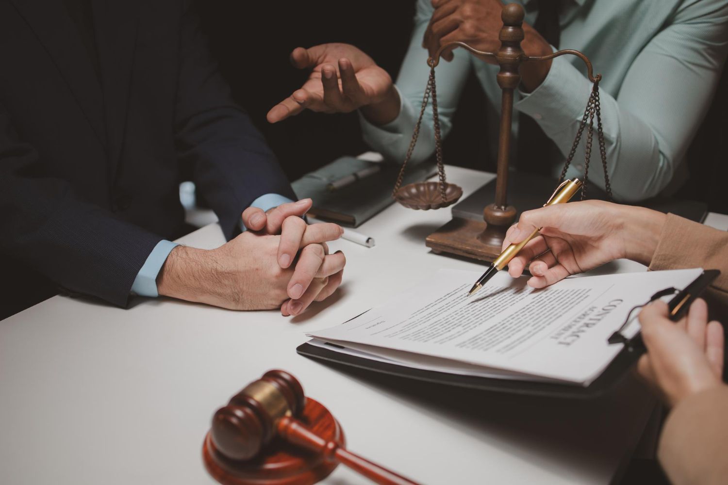 People at a desk; one signing a document, scales, gavel.