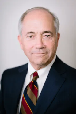 Man in suit, white shirt, and striped tie; smiling slightly, headshot.