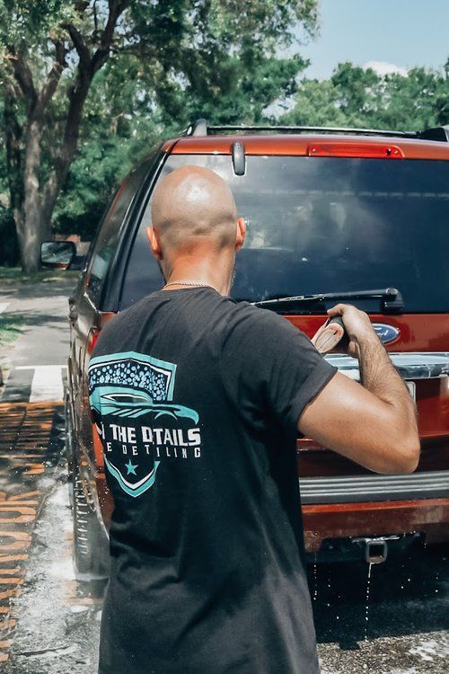 A man in a black shirt is washing a red suv.