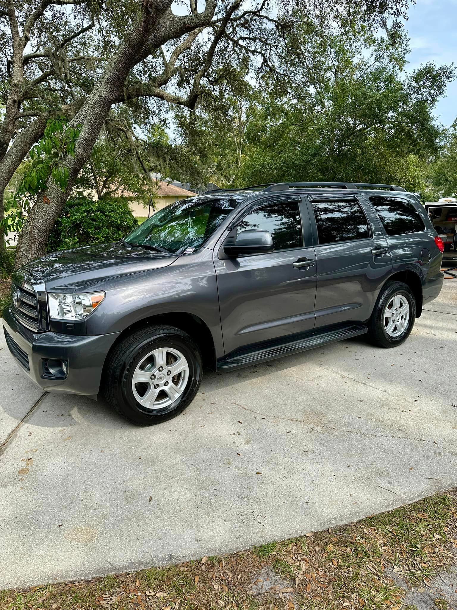A toyota sequoia is parked in a driveway next to a tree.