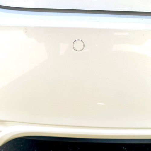 A white car with a parking sensor on the back bumper.