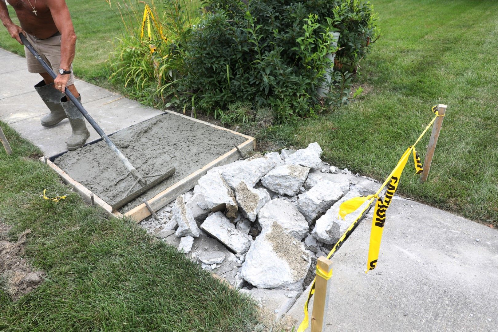 A man is spreading concrete on a sidewalk with a rake.