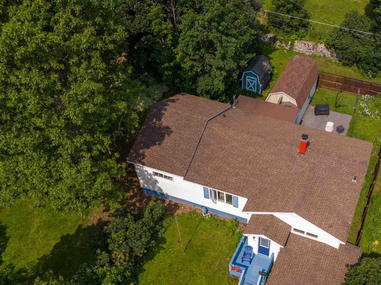 An aerial view of a white house with a brown roof surrounded by trees.