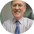 A man wearing glasses and a tie is smiling for the camera.