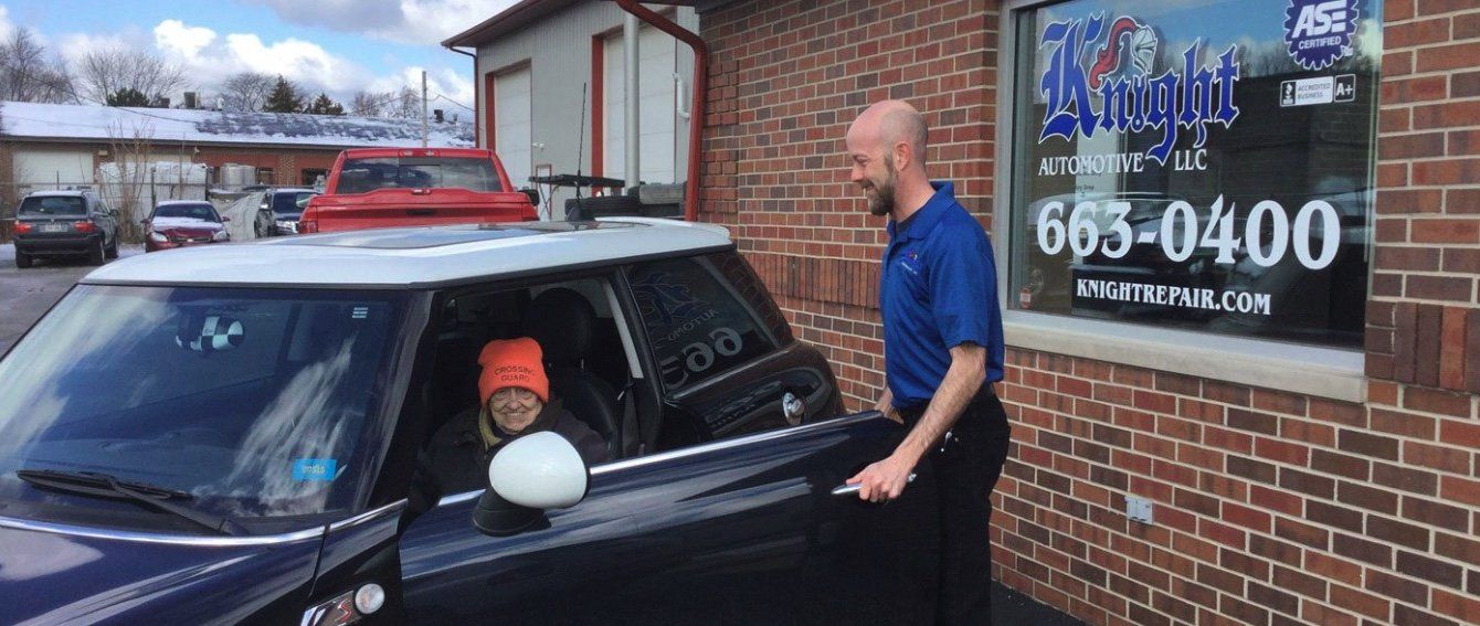 A man is standing next to a car with a child sitting in the driver 's seat.