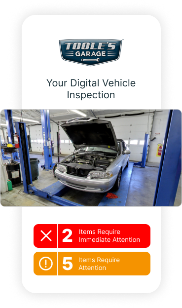 A car with its hood up is on a lift in a garage.