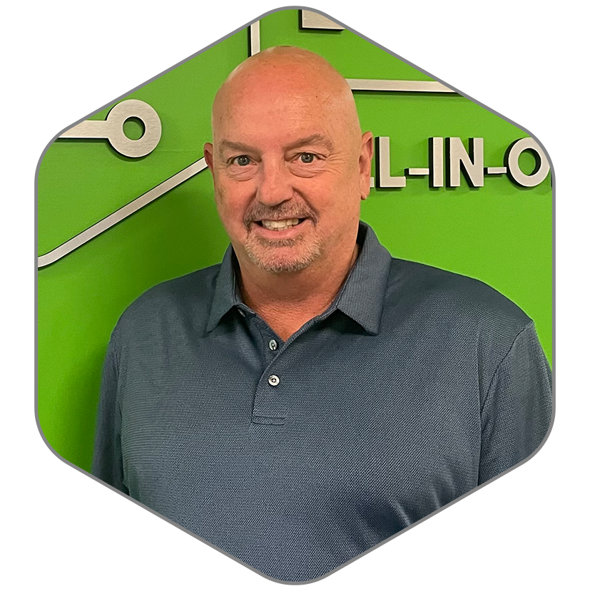 A man in a blue shirt is smiling in front of a green wall.