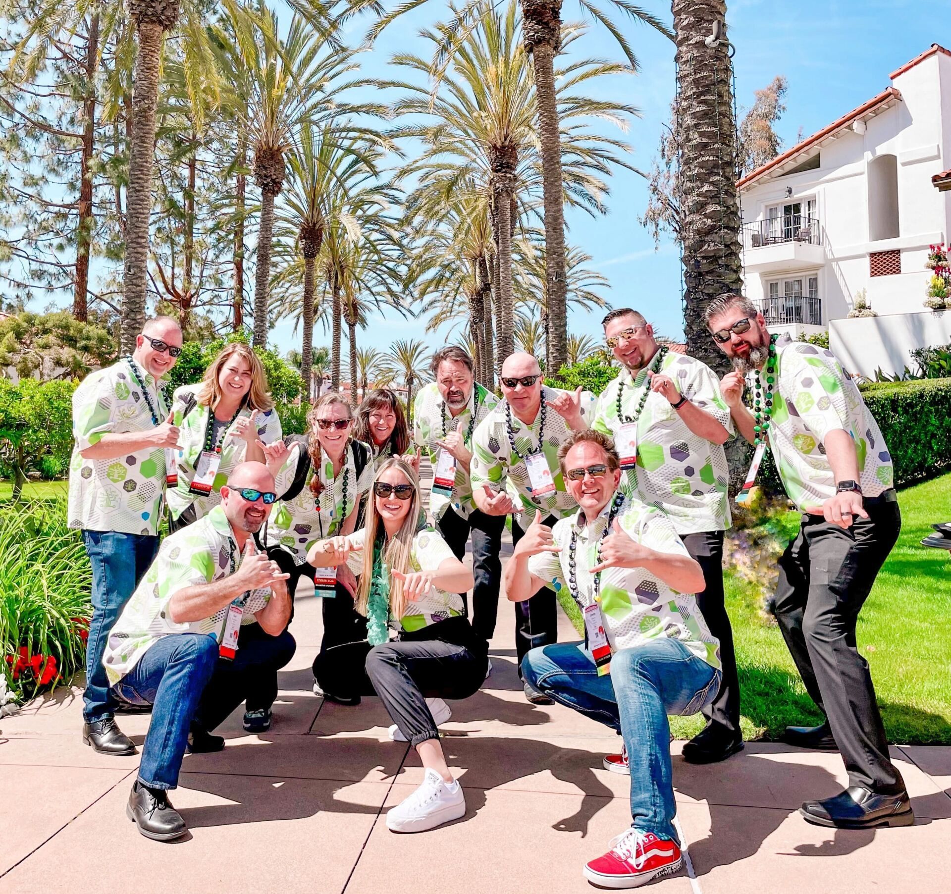 Group of people posing outdoors in matching green shirts on a sunny palm-lined walkway
