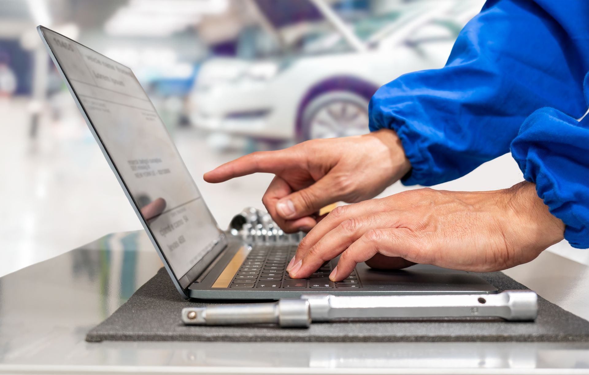 Up close to technician typing on a laptop in auto repair garage | KUKUI