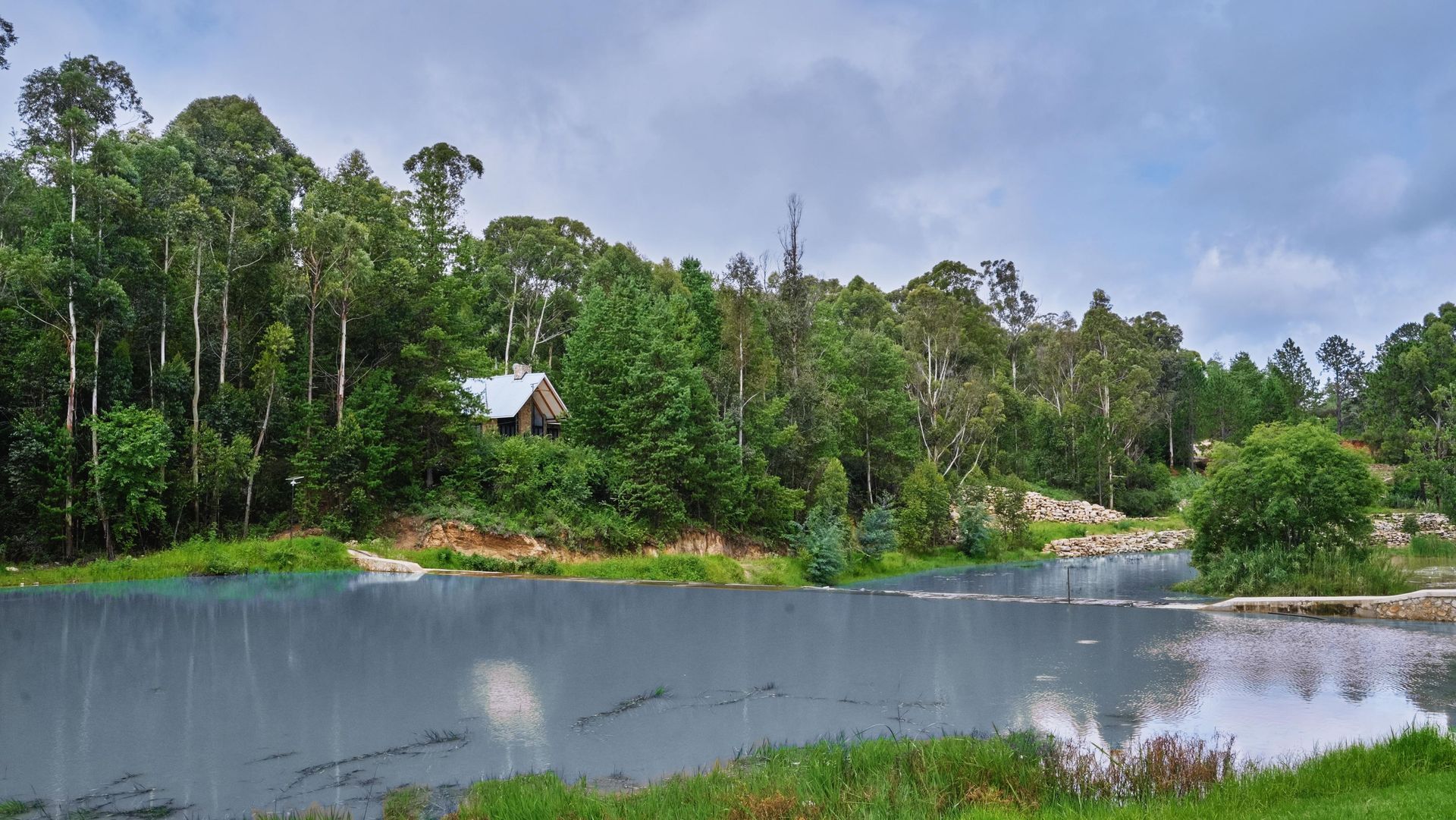 A small house sits on the shore of a lake surrounded by trees.